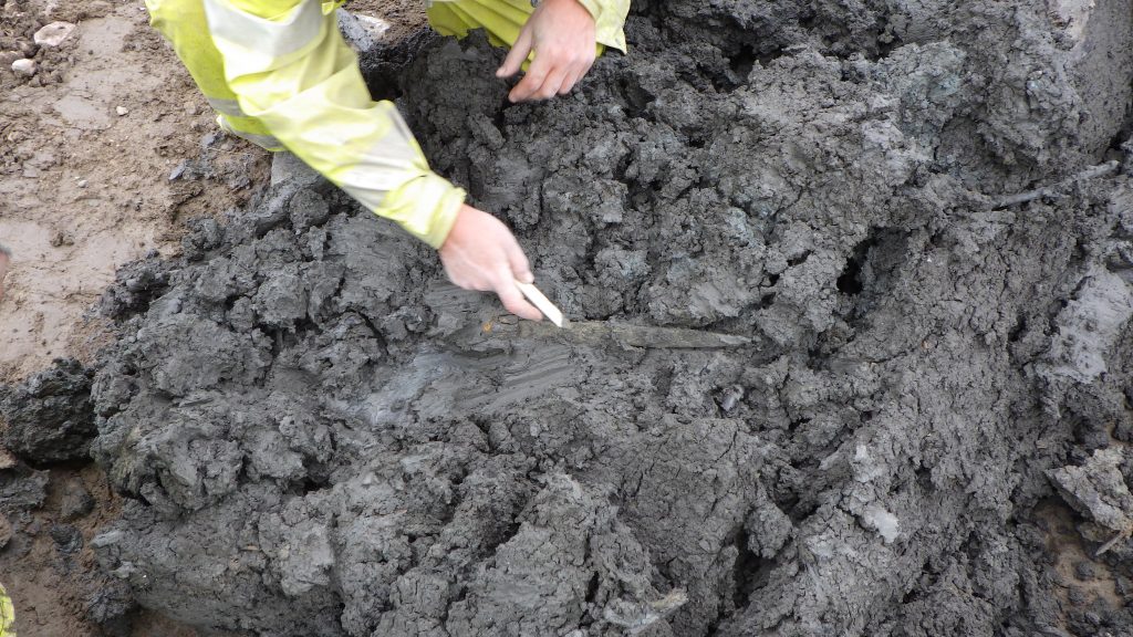 En arkeolog gräver fram ett svärd eller kniv ur lermassorna.