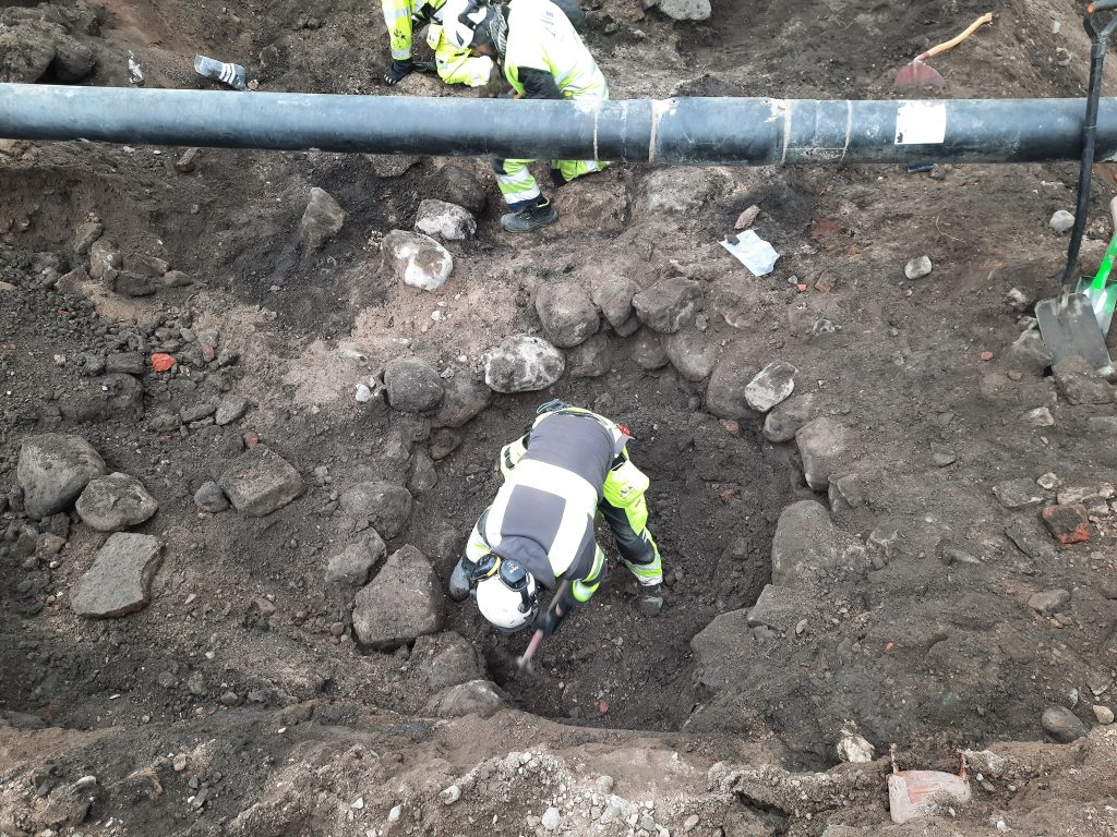 Arkeolog gräver fram en brunn i början av undersökningen.