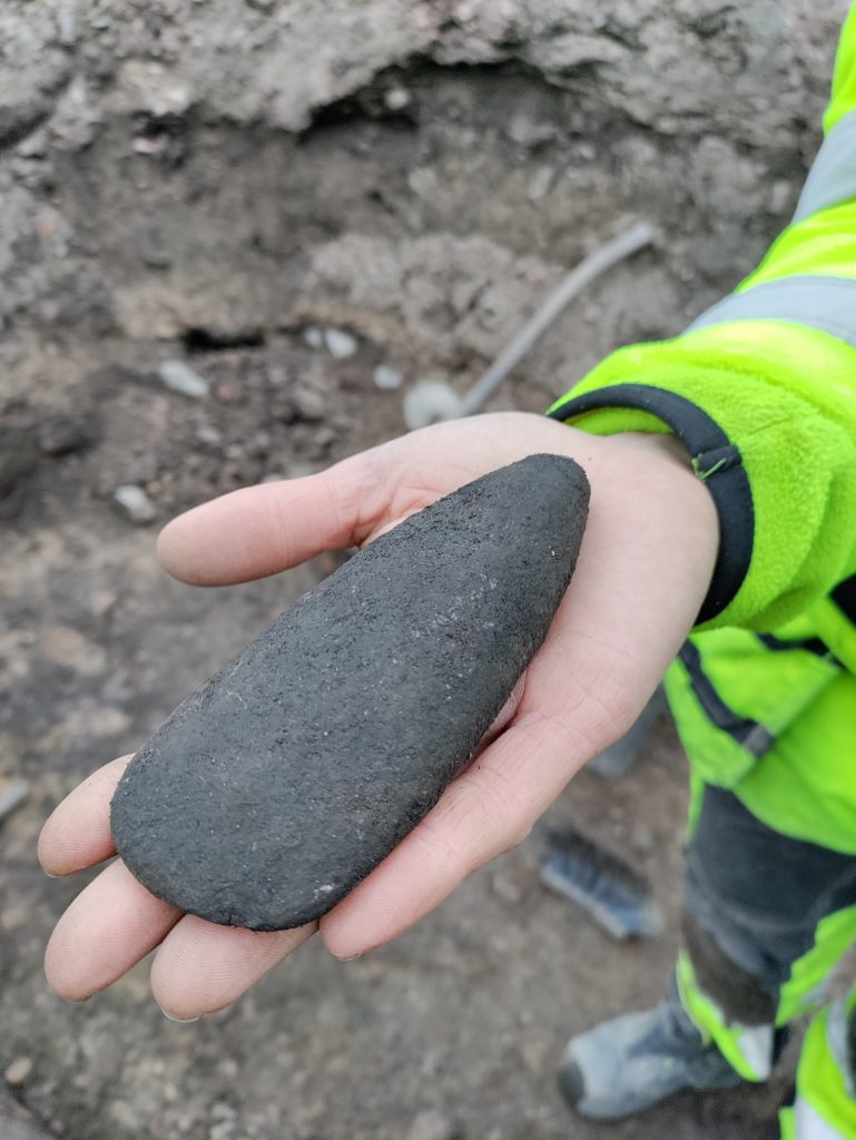 En hand som håller i en trindyxa av sten.