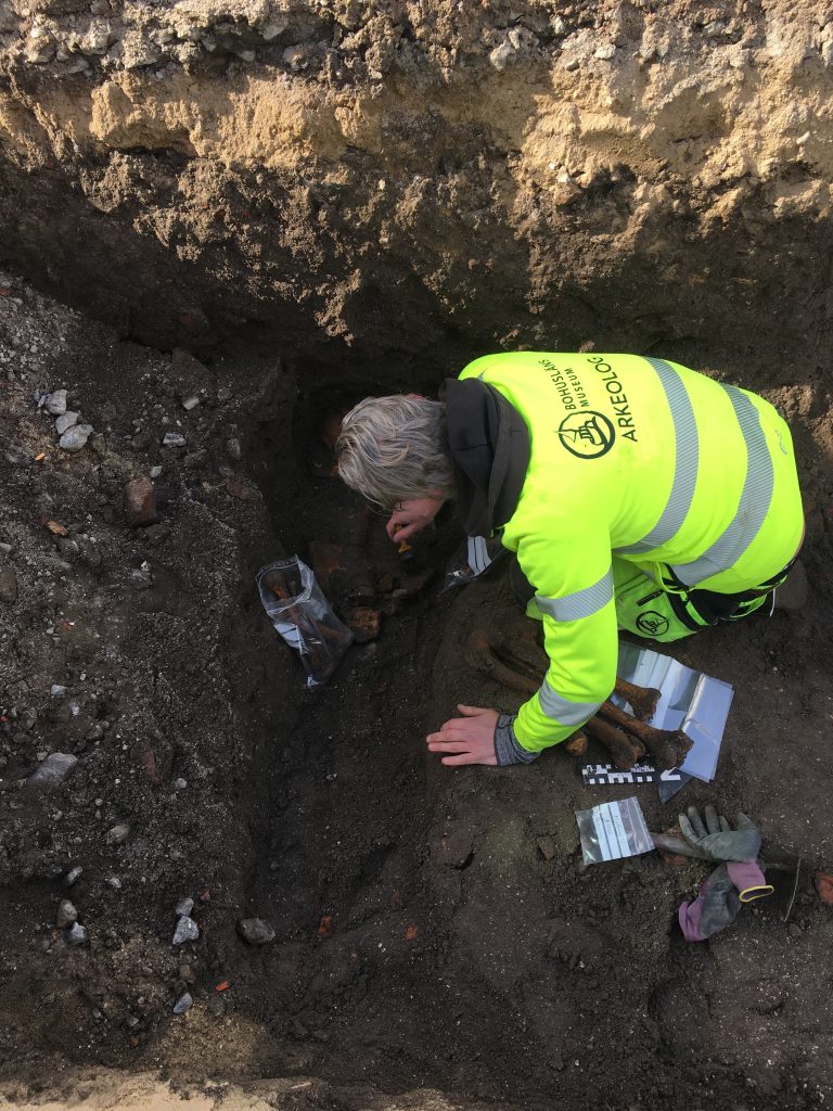 En arkeolog i gula fältkläder undersöker en grav.
