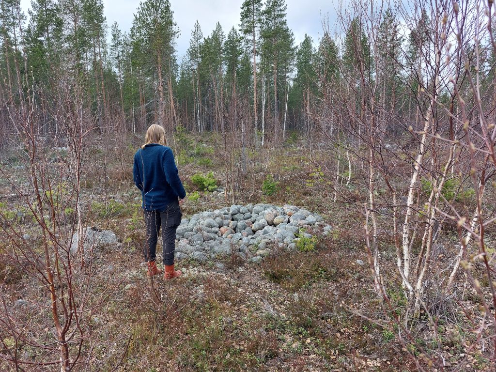 En person står vid ett stenröse vid en skog.