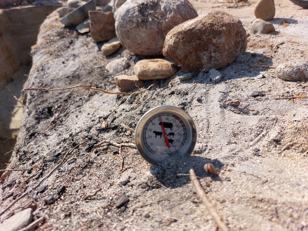 En termometer står i solen på marken, visar över 50 grader.