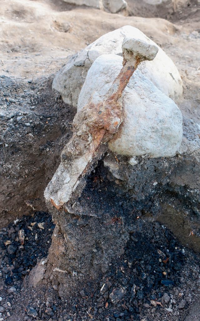 Hälften av ett svärd som står mot en sten och mörk mark.