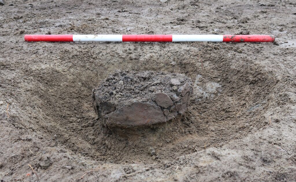 En bit av en urna i jorden med röd-vit-randig måttstock ovanför.