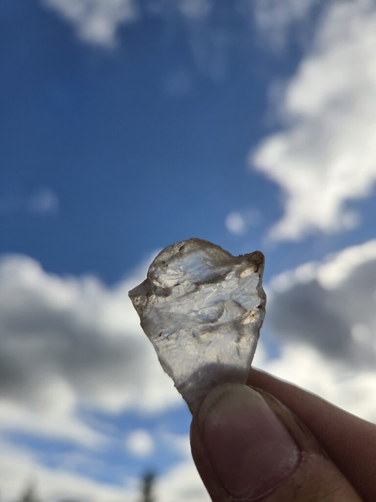 Vacker genomskinlig bit av bergkristall med blå himmel och vita moln bakom. 